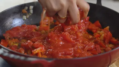 Chopping tomatoes in a skillet for a homemade sauce with bell peppers.