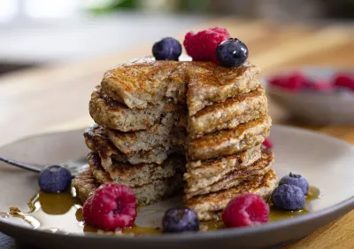 A stack of pancakes topped with fresh berries and syrup on a plate, with a rustic wood background.