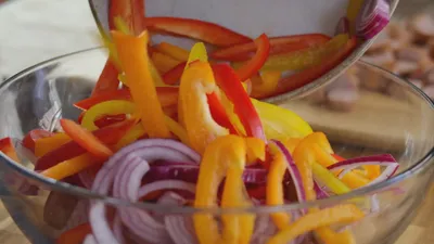 Fresh sliced bell peppers and onions being poured into a glass bowl.