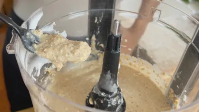 Close-up of pancake batter in a food processor with a spoonful of creamy mixture being lifted out.
