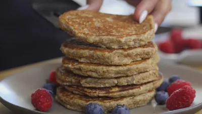 Stack of golden pancakes with fresh raspberries and blueberries on a plate being served.