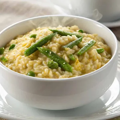 Risotto agli Asparagi (Asparagus Risotto) topped with fresh herbs served in a white bowl.