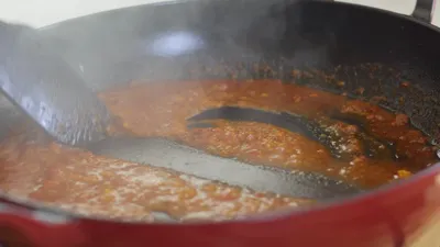 Steaming tomato sauce simmering in a red pan, being stirred with a large black spatula.