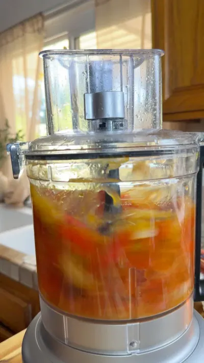 Food processor blending colorful vegetables in a sunny kitchen setting.