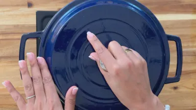 Hands closing a blue Dutch oven lid on a wooden countertop.