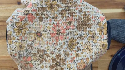 Floral-patterned cloth covering a dutch oven, resting on a wooden table.