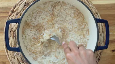 Hand stirring fluffy basmati rice in a pot on a woven mat background.