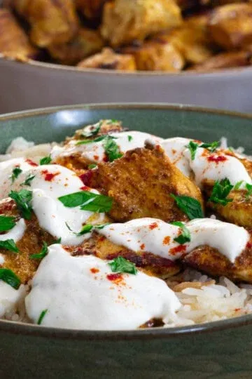 Garlic yogurt marinated chicken kebab over rice topped with creamy sauce and herbs in a bowl.
