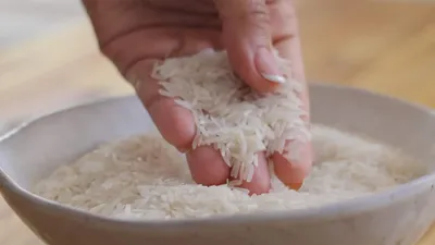 Hand holding Basmati rice over bowl, showcasing raw grains' quality and texture.