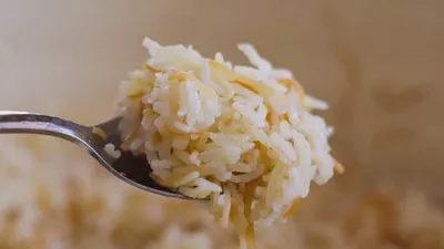 Close-up of a forkful of cooked Lebanese vermicelli rice with golden vermicelli, showcasing texture and color contrast.