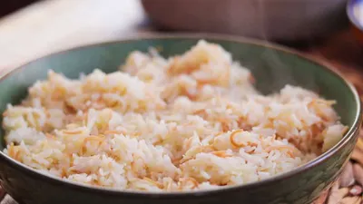 A bowl of freshly cooked Lebanese vermicelli rice with vermicelli, steaming and ready to serve, in a green ceramic dish.
