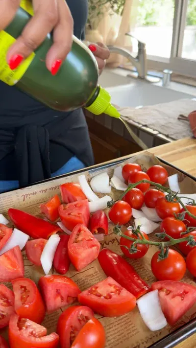 Preparing fresh tomatoes, onions, bell peppers on a baking tray with olive oil drizzle for roasting.