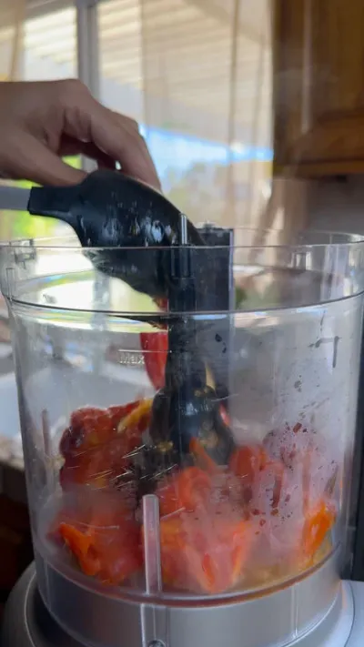 Hand operating food processor filled with chopped tomatoes.