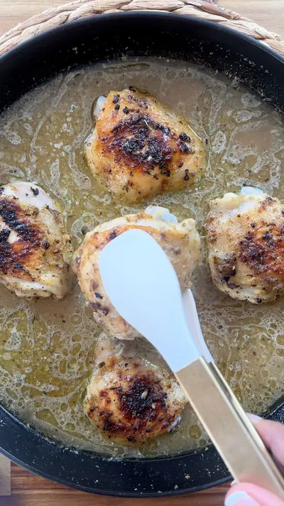 Cooking seasoned chicken thighs in a skillet with a spatula.