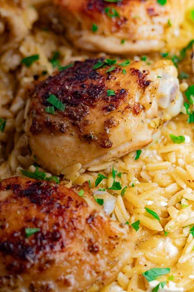 Close-up of Greek Chicken Orzo Bake served on a bed of orzo pasta, garnished with fresh parsley.