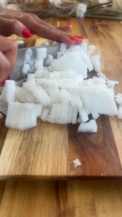 Chopping white onions on a wooden board with a sharp knife.