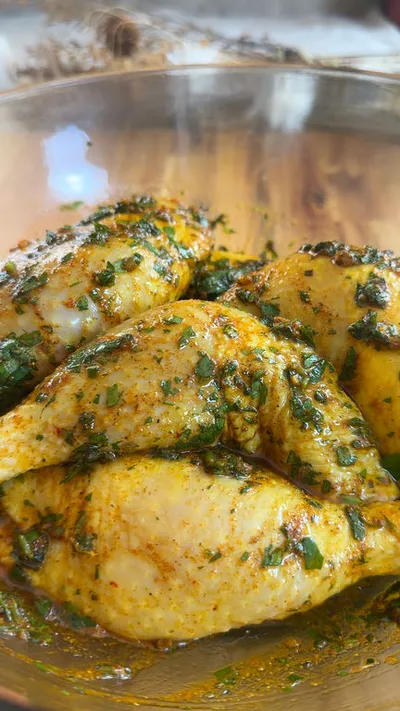 Marinated chicken pieces in a bowl with fresh herbs and spices in a bowl.