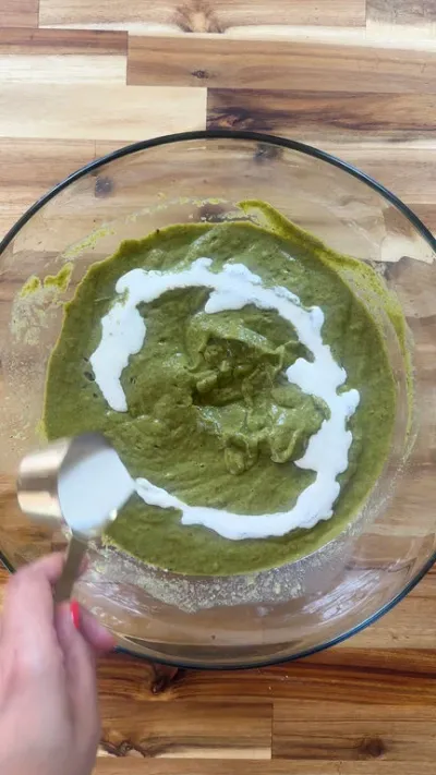 Pouring cream into a bowl of green soup.