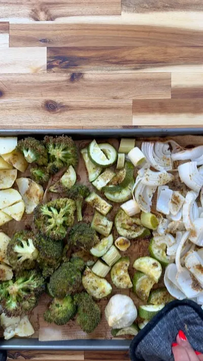 Roasted vegetables on a tray including broccoli, onions, and zucchini, seasoned with spices.