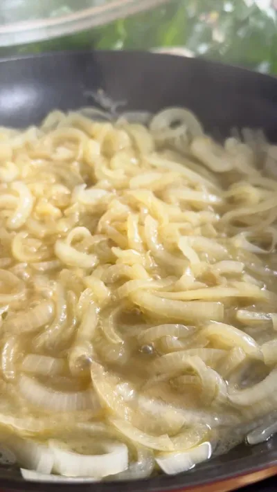 Sliced onions simmering in a pan, cooking in oil, with bubbles forming around them.
