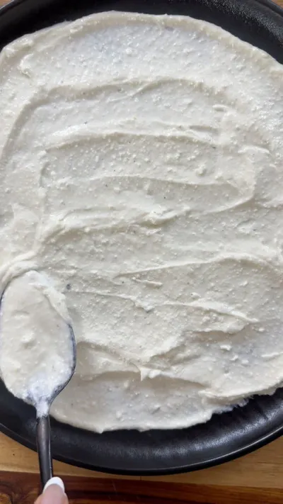Spreading whipped feta with a spoon on a black round pan.