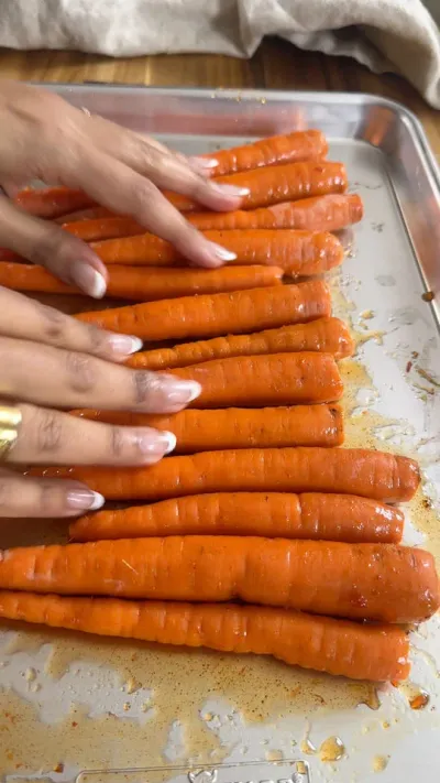 Hands arranging seasoned carrots on a baking tray.