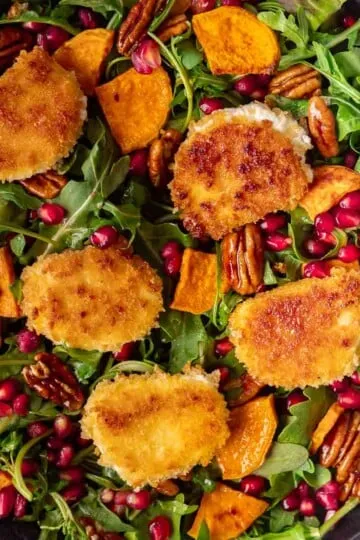 Crispy goat cheese salad with arugula, pecans, pomegranate seeds, and roasted sweet potato slices.