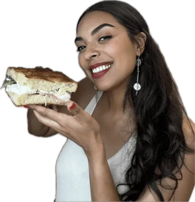 Smiling woman holding a large sandwich with layers of meat and lettuce.