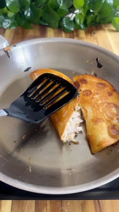 Chicken taco being cooked in a pan with a spatula on a wooden surface background.