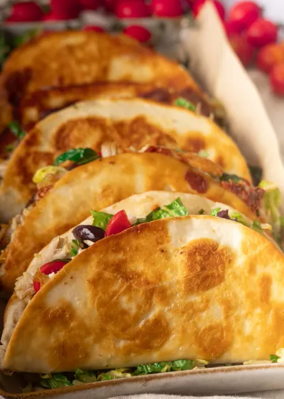 Close-up of Greek crispy chicken tacos filled with lettuce, tomatoes, olives, and shredded chicken.
