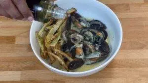 Mussels in creamy sauce with crispy fries in a bowl, finished with a drizzle of olive oil.