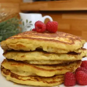 Stack of homemade pancakes topped with fresh raspberries on a white plate.