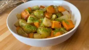 Bowl of roasted potatoes and sweet potatoes with green pesto sauce on a wooden table.