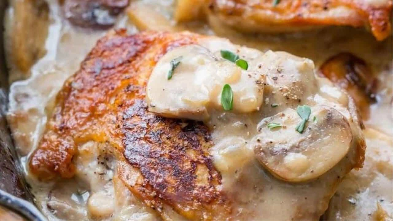 Creamy garlic mushroom chicken with crispy skin in sauce, garnished with herbs.