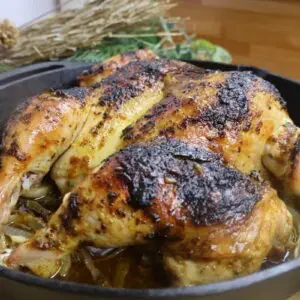 Roasted chicken in a cast iron skillet with crispy skin, seasoned to perfection. Ideal for a savory homemade meal.