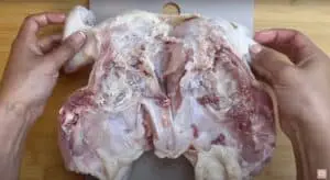 Raw chicken being prepared for spatchcocking on a cutting board.