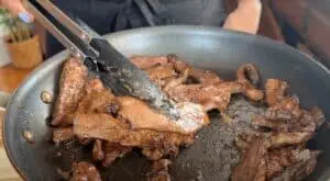 Cooking juicy beef strips in a frying pan with tongs, ready for a delicious meal.