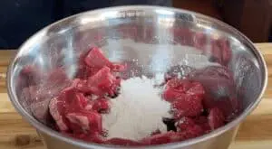 Raw beef cubes with flour in a mixing bowl ready for cooking preparation.