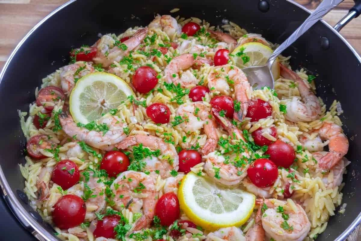 Shrimp orzo with cherry tomatoes, lemon slices, and fresh parsley in a skillet, ready to serve.