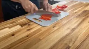 Person slicing red bell pepper on a cutting board in a kitchen.