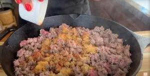 Seasoning ground beef in a cast iron skillet for cooking.
