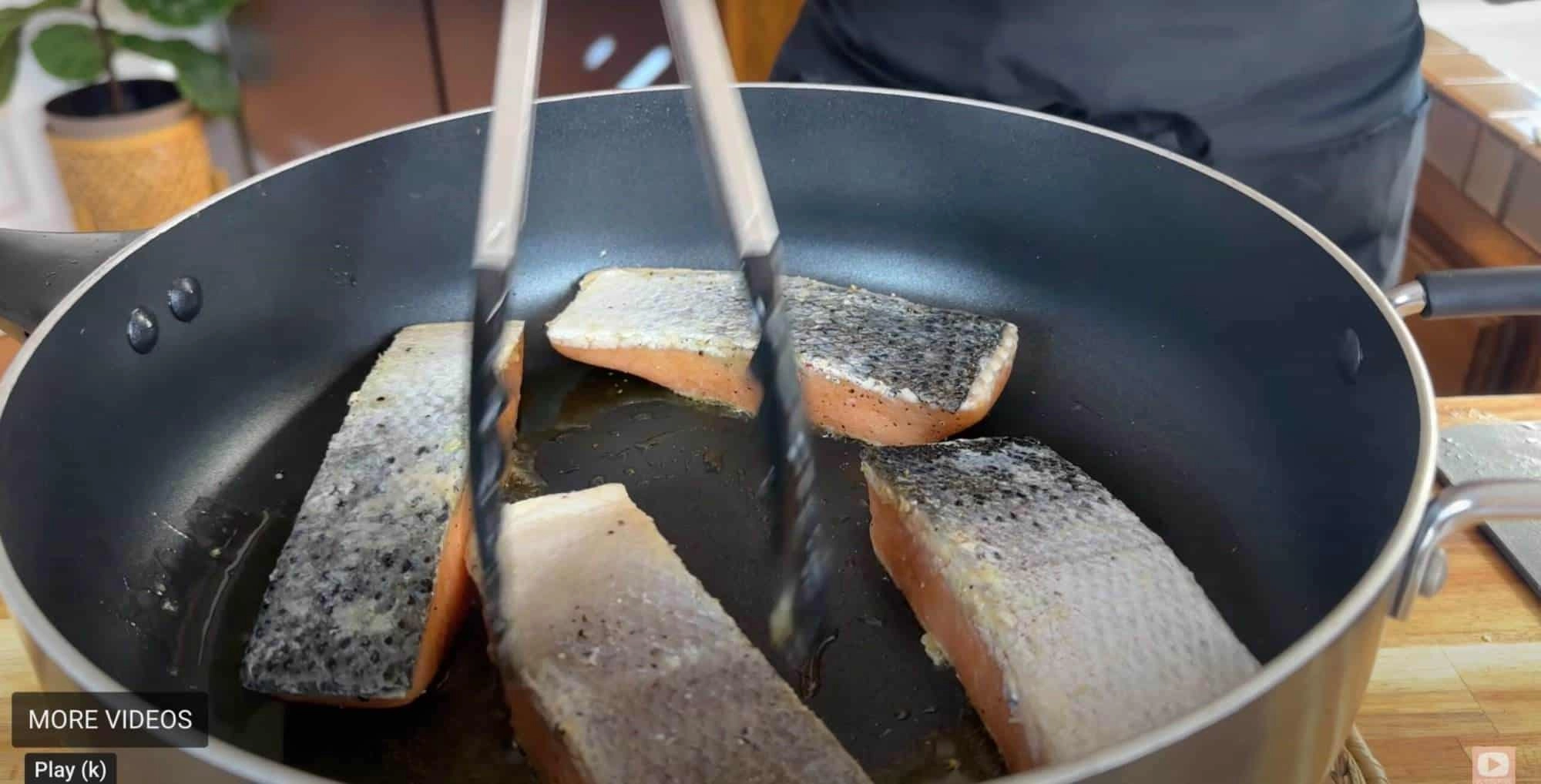 Cooking salmon fillets in a non-stick pan, skin-side down, with tongs.
