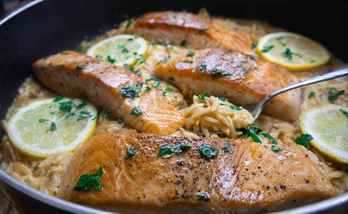Pan-seared salmon with orzo, lemon slices, and herbs, served in a skillet for a deliciously savory meal.