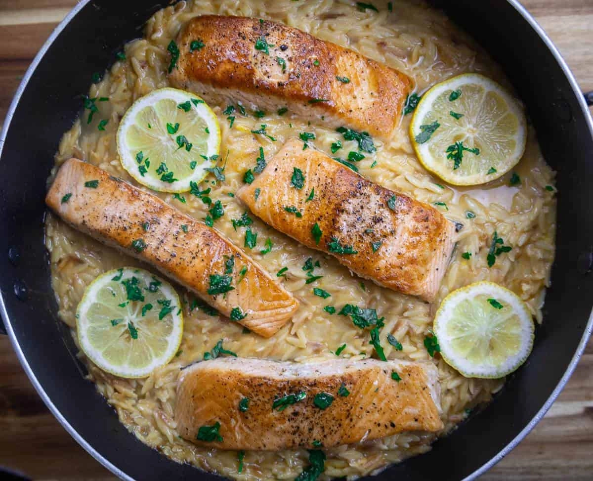 Pan-seared salmon with creamy lemon orzo, garnished with parsley and lemon slices in a skillet.