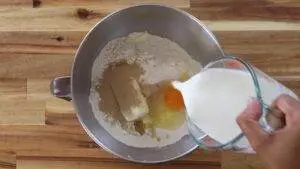 Mixing milk into dough ingredients in a metal bowl for baking on a wooden surface.