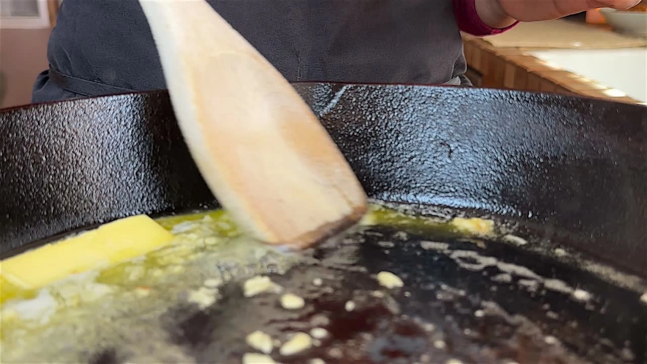 Melting butter in a cast iron skillet with a wooden spatula stirring in garlic.