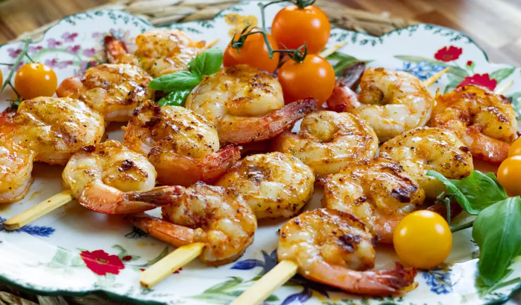 Grilled shrimp skewers garnished with fresh basil and cherry tomatoes on a floral plate.