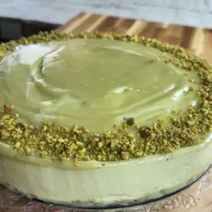 Creamy no bake pistachio cake with a smooth green frosting and crushed pistachio topping on a wooden board.