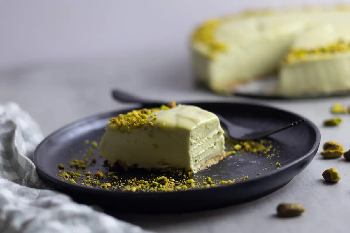 Slice of creamy No-Bake Mascarpone Pistachio Cheesecake on a black plate with scattered nuts.