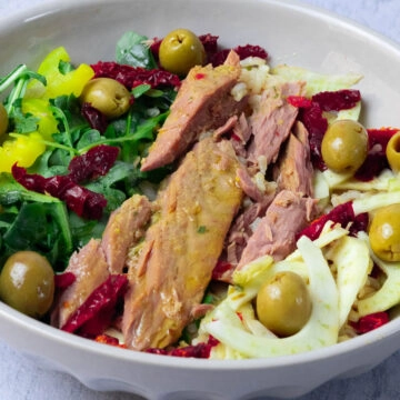 Tuna and rice salad bowl with olives, arugula, sun-dried tomatoes, and pepper rings in a bowl on a light background.